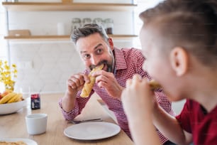 A mature father with small son indoors sitting at the table, eating pancakes.