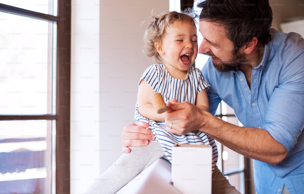 Père mûr avec une petite fille jouant avec une maison en carton à l’intérieur à la maison.