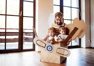 父親と幼児の子供が自宅の屋内でカートン飛行機で遊んで、コンセプトを飛ばす。