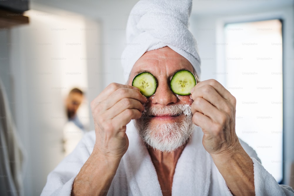Um homem idoso com pepino na frente dos olhos no banheiro dentro de casa.