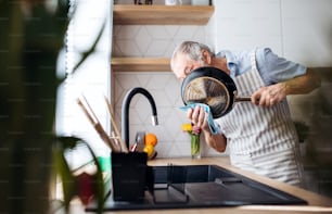 A senior man indoors in kitchen at home, washing up a pan after cooking.