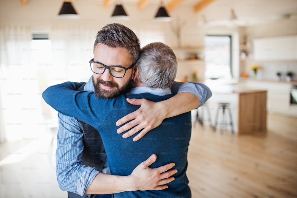 Un figlio adulto e un padre anziano in piedi in casa a casa, abbracciati.