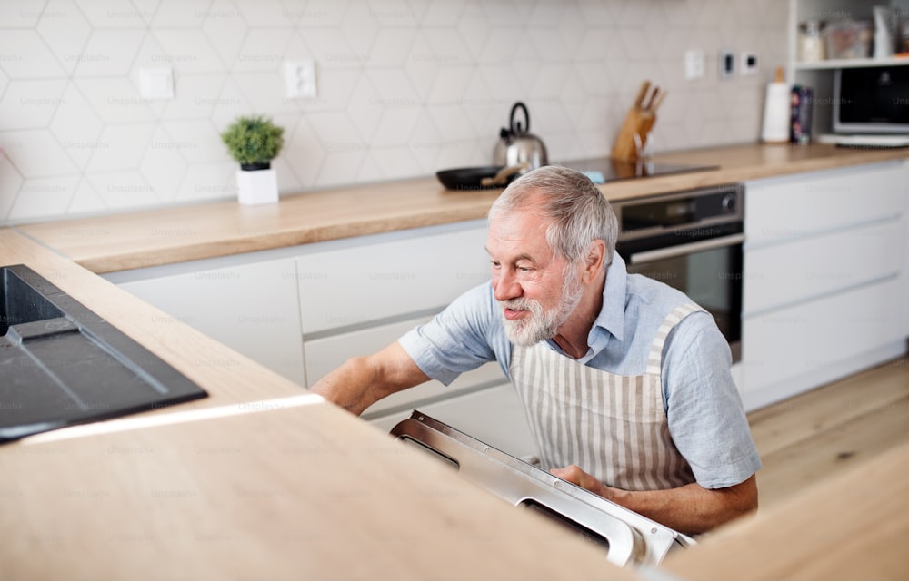 A senior man indoors in kitchen at home, loading or unloading dishwasher.