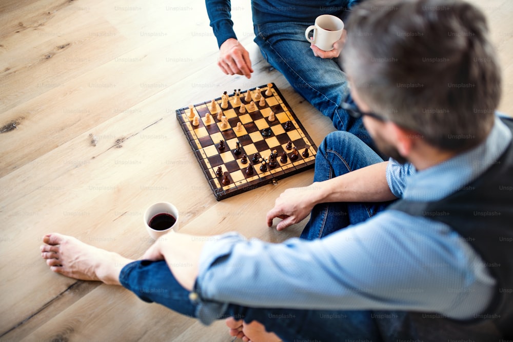 쾌활한 성인 힙스터 아들과 선배 아버지가 집 실내 바닥에 앉아 체스를 두는 모습의 중간부.