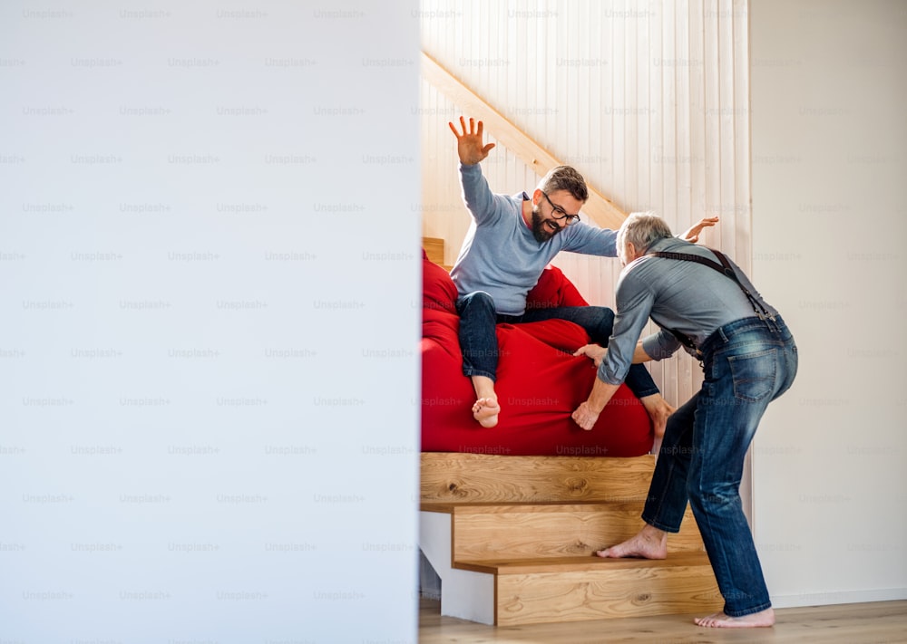 성인 힙스터 아들과 선배 아버지가 집 안에서 계단을 미끄러지며 즐거운 시간을 보내고 있다.