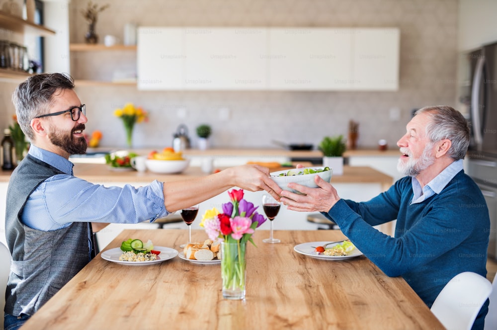 大人の流行に敏感な息子と年配の父親が自宅の屋内のテーブルに座って昼食をとる。