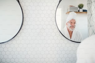家の屋内のバスルームで朝の日課をしている年配の男性が鏡を見ている。スペースをコピーします。