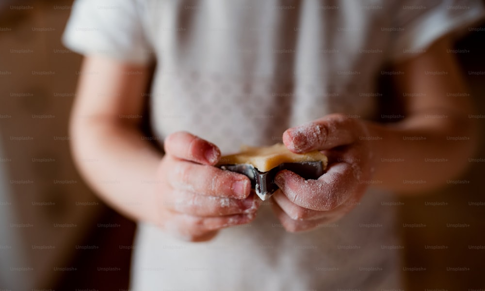 A midsection of small toddler boy making cakes at home, a close-up of hands holding a biscuit cutter.