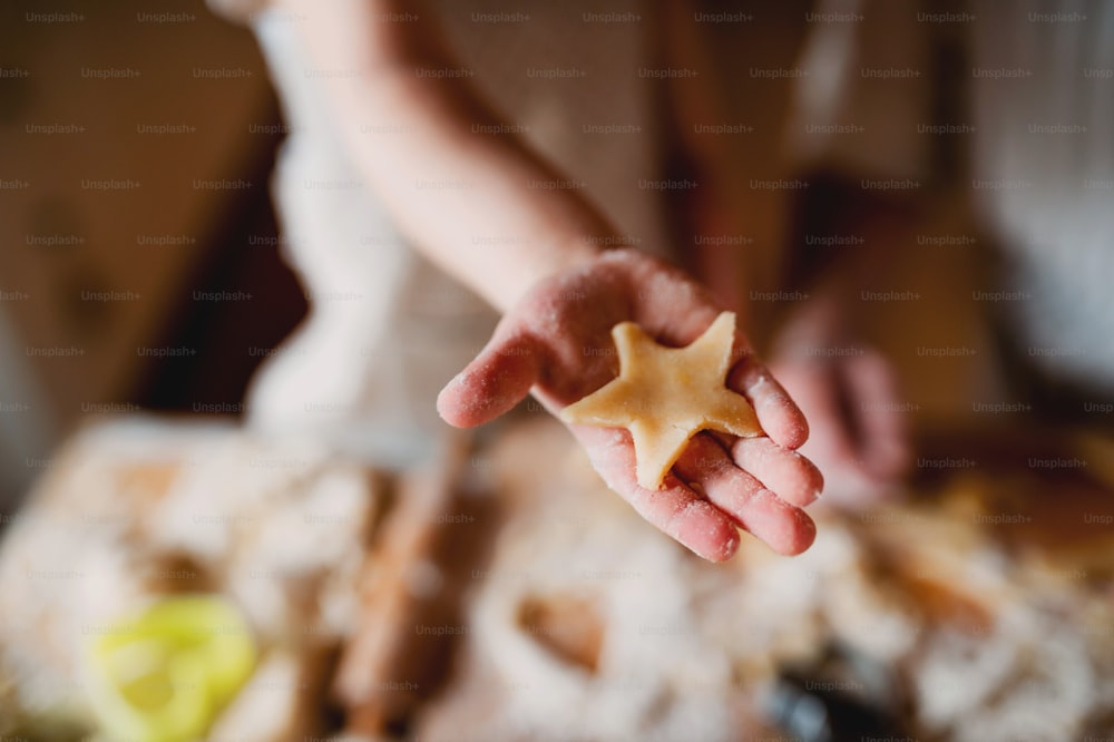 A midsection of small toddler boy making cakes at home, a close-up of a hand holding a biscuit.