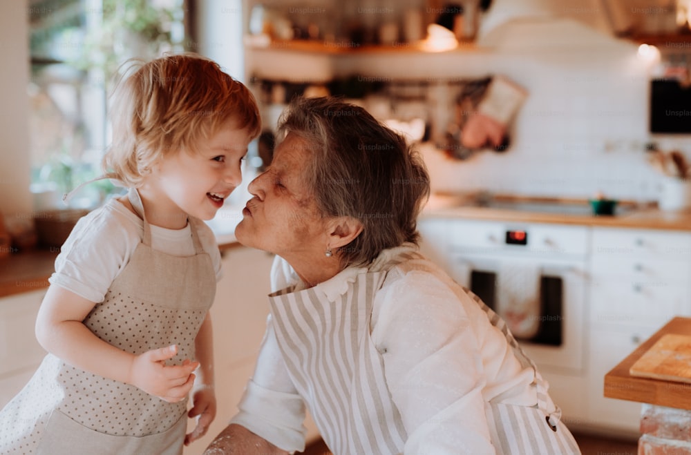 Feliz bisabuela mayor con un niño pequeño haciendo pasteles en casa, besándose.