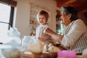 Glückliche ältere Urgroßmutter mit kleinem Kleinkind, das zu Hause Kuchen backt.