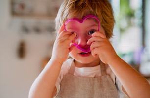 A small toddler boy looking through a pink cake cutter at home, having fun.