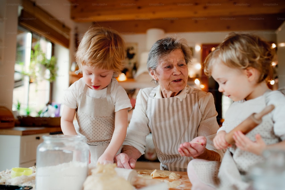 Glückliche ältere Urgroßmutter mit kleinen Kleinkindern, die zu Hause Kuchen backen.