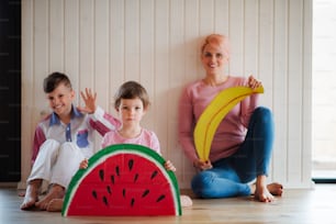 Eine junge Frau mit zwei Kindern mit großen Spielzeugfrüchten sitzt zu Hause auf dem Boden.