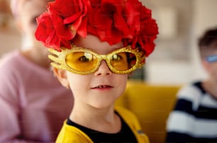 Una niña pequeña con la familia divirtiéndose en casa, con gafas de fiesta y diadema de flores.