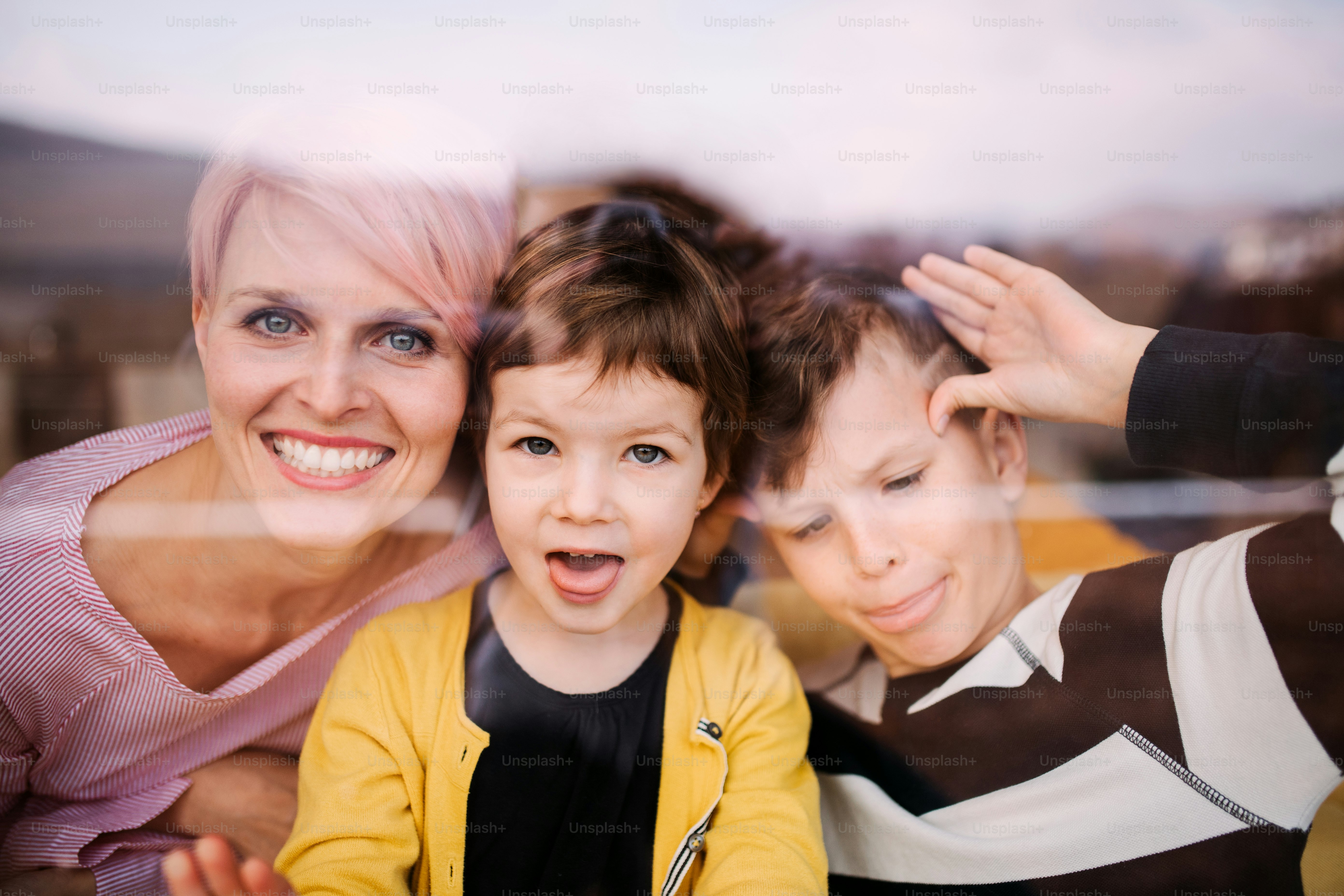 A portrait of young woman with two children at home, looking at camera. Shot through glass.