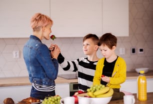 Una giovane donna con due bambini felici che mangiano frutta in una cucina.