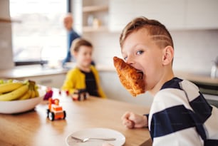 Two cheerful small children with mother in a kitchen, eating.