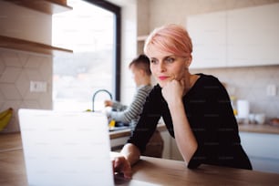 A young woman with a small son using laptop in a kitchen at home, working.