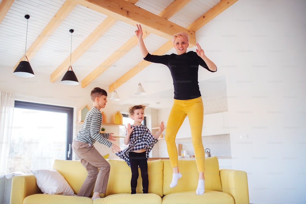 A young woman with two children jumping on a sofa at home, having fun.