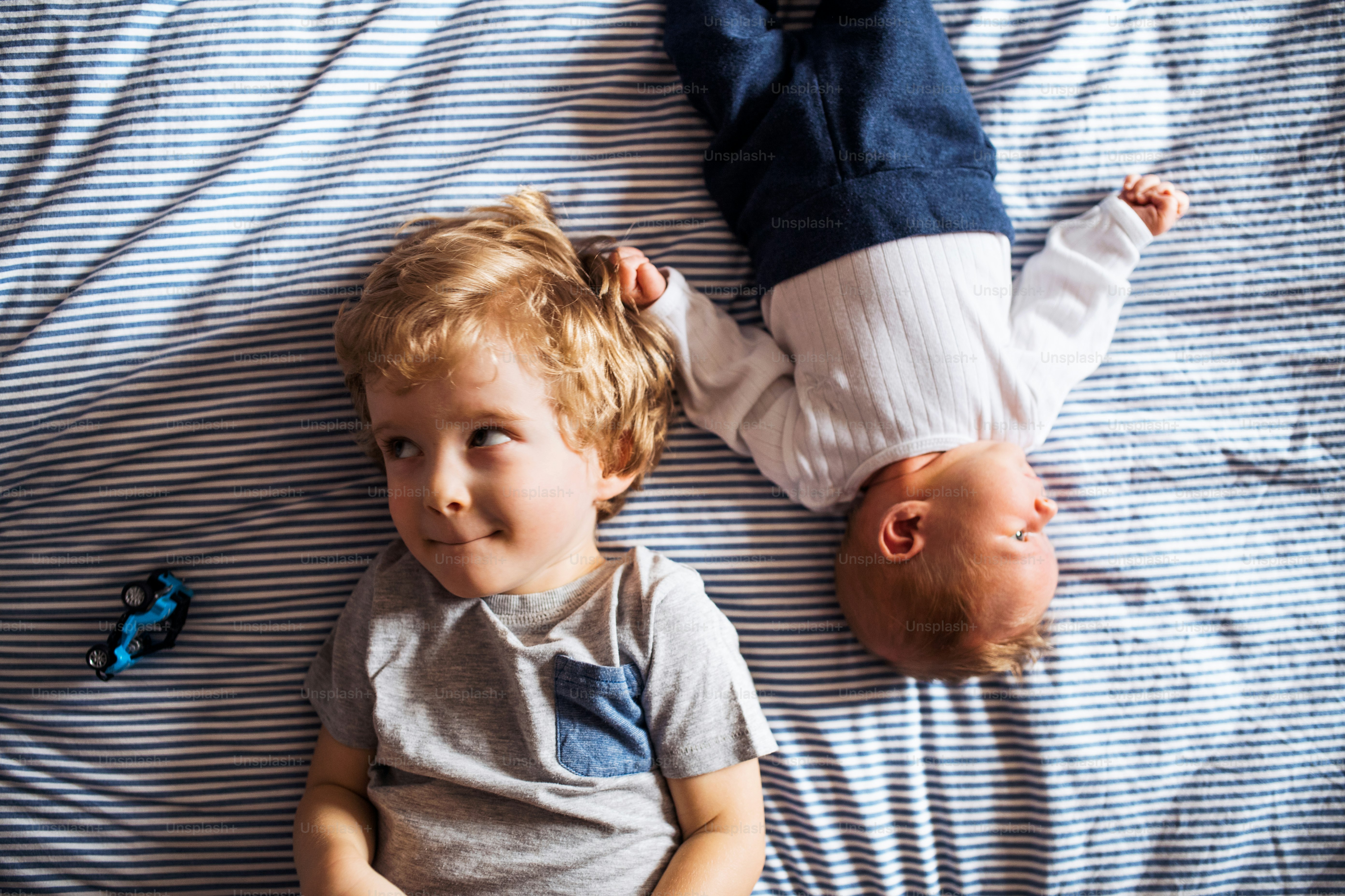 Una vista superior de un niño pequeño con un hermanito recién nacido en casa, acostado en la cama.