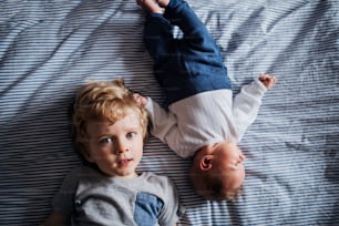 Eine Draufsicht auf einen kleinen kleinen Jungen mit einem neugeborenen kleinen Bruder zu Hause, der sich auf das Bett legt.