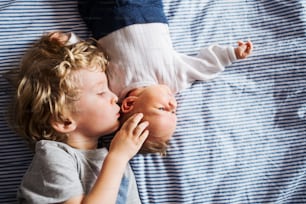Uma vista superior do menino pequeno com um irmão recém-nascido em casa, deitado na cama.