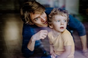 A happy father holding a toddler son at home. Shot through glass.