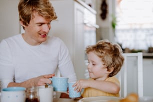 A young father with a toddler son eating breakfast indoors at home.