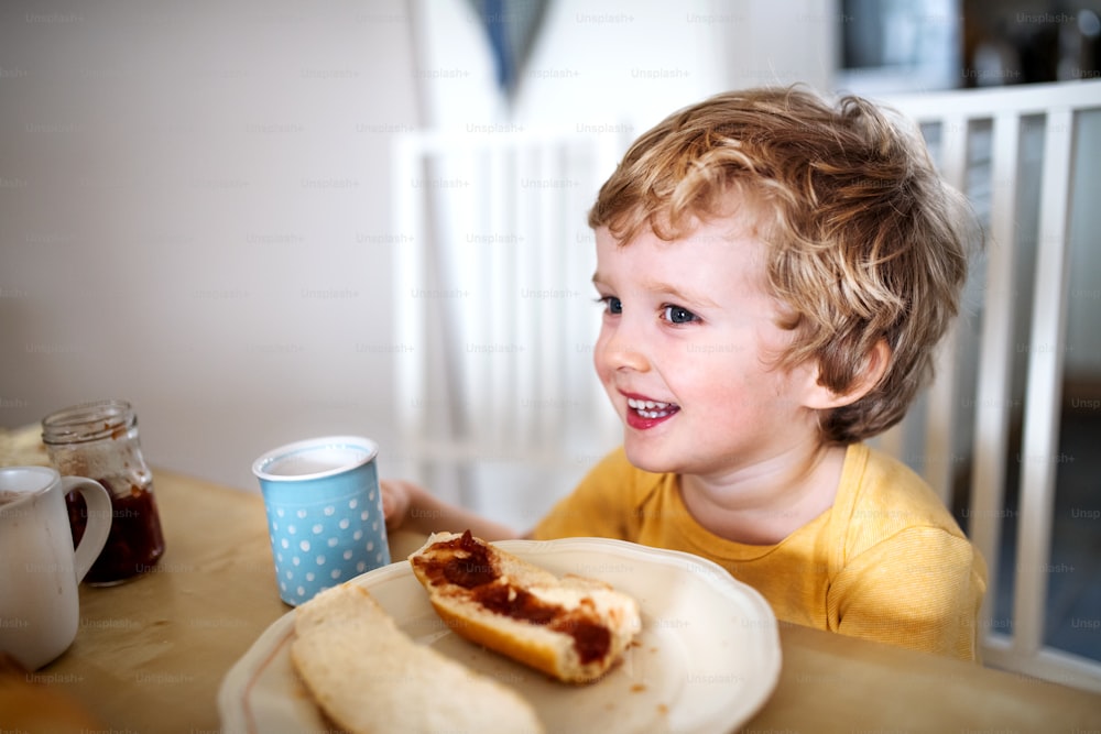 Uma vista frontal de um menino feliz sentado à mesa em casa, comendo.
