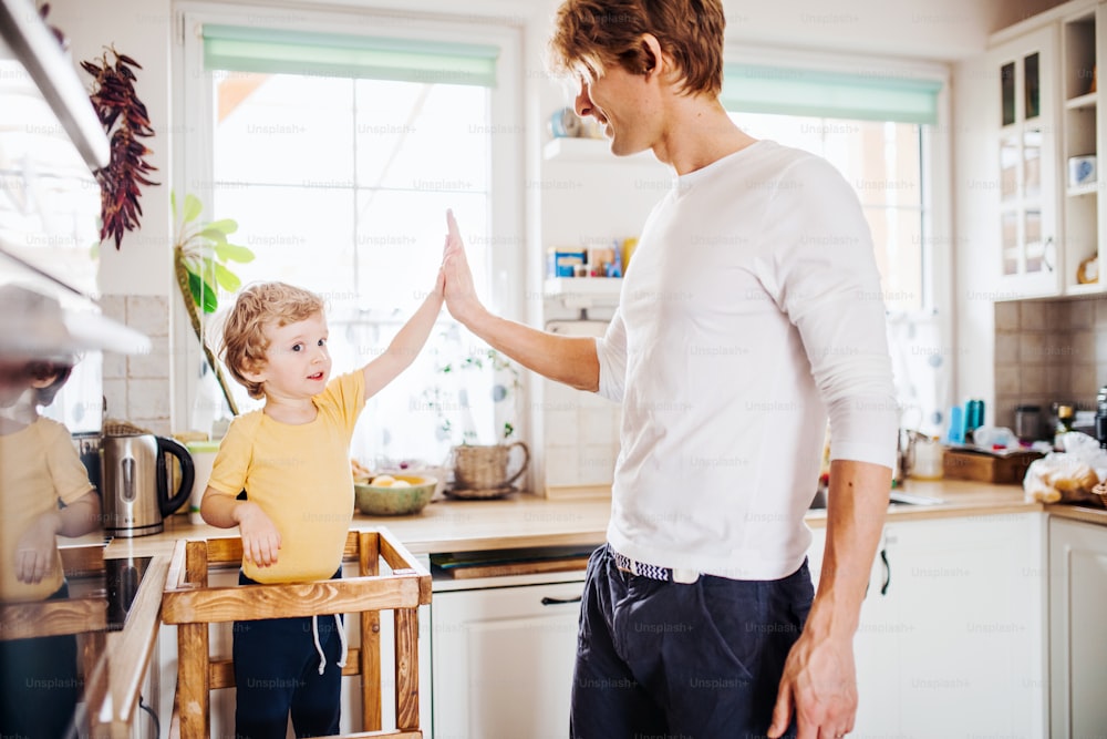 A young father with a toddler son spending time in a kitchen at home, giving high five.