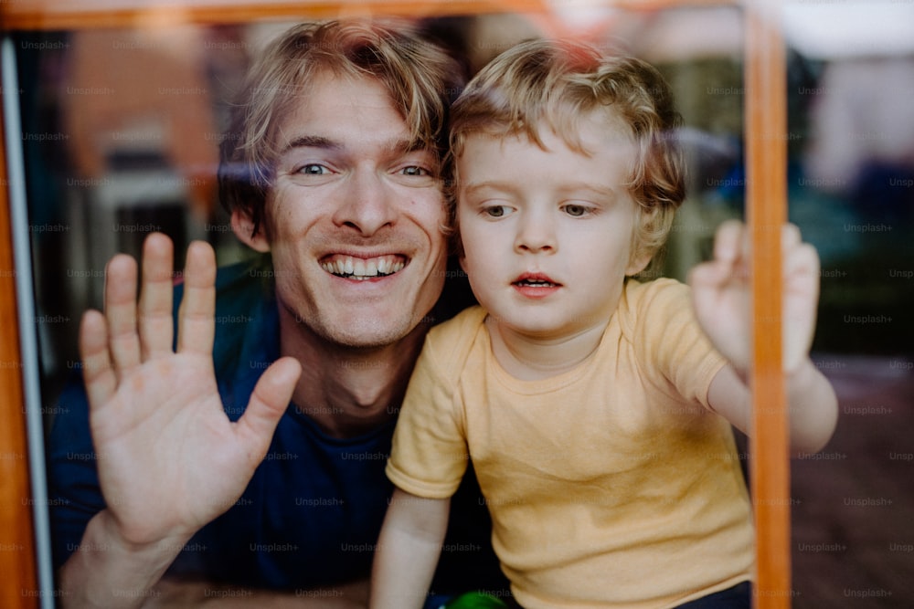 A happy father with a toddler son at home, looking at camera. Shot through glass.