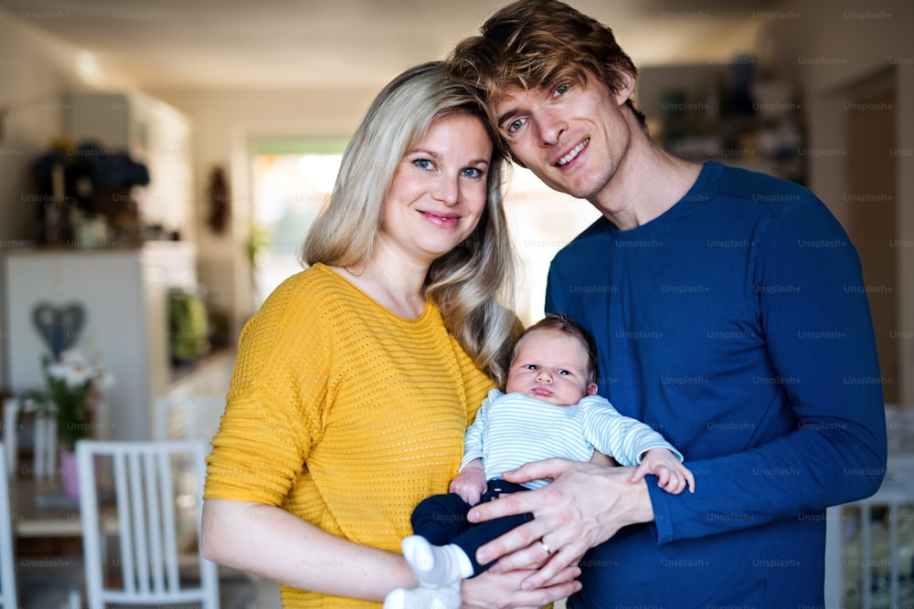 Beautiful young parents holding a newborn baby at home.