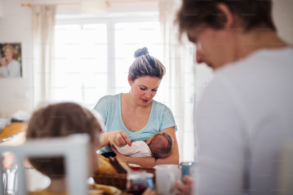 Young parents with a newborn baby and small toddler son sitting at the table at home.