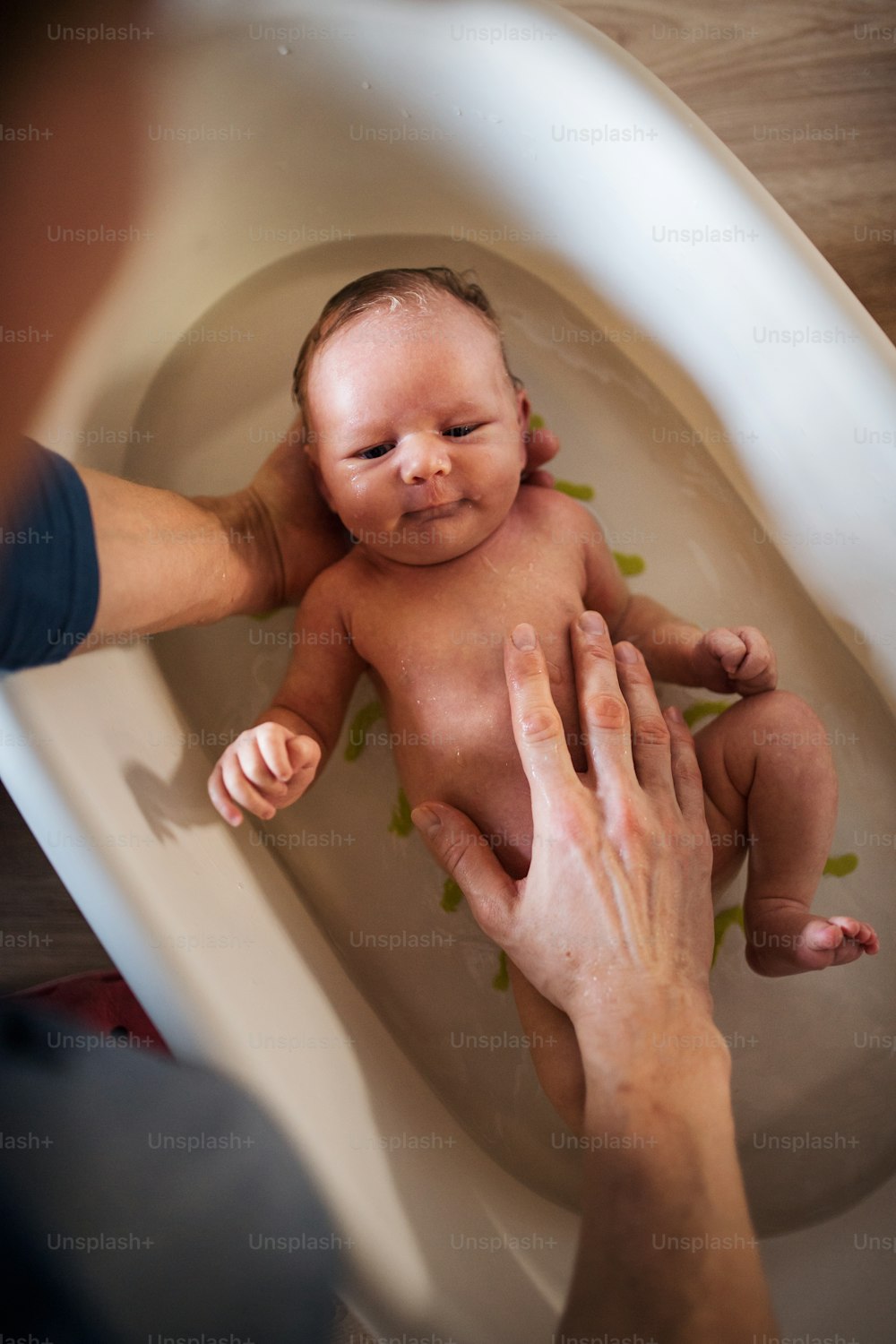 Top view of unrecognizable parent giving a happy newborn baby a bath at home.