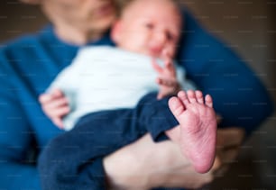 Ein Vater, der ein Neugeborenes zu Hause hält, eine Nahaufnahme des nackten Fußes im Vordergrund.