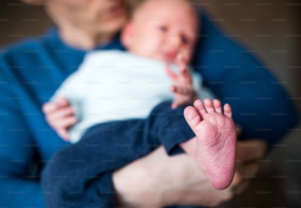 A father holding a newborn baby at home, a close-up of bare foot in the foreground.