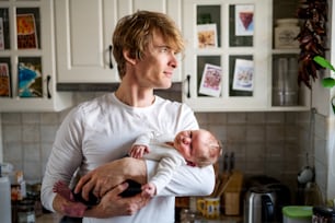 A young father holding a newborn baby in kitchen at home.