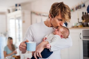 A young father holding a newborn baby in kitchen at home, kissing.