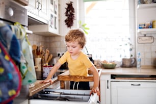 Un joyeux petit garçon debout dans une cuisine à la maison.