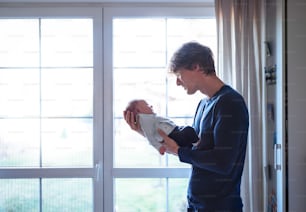 Um jovem pai feliz segurando um bebê recém-nascido em casa, olhando para ele. Espaço de cópia.