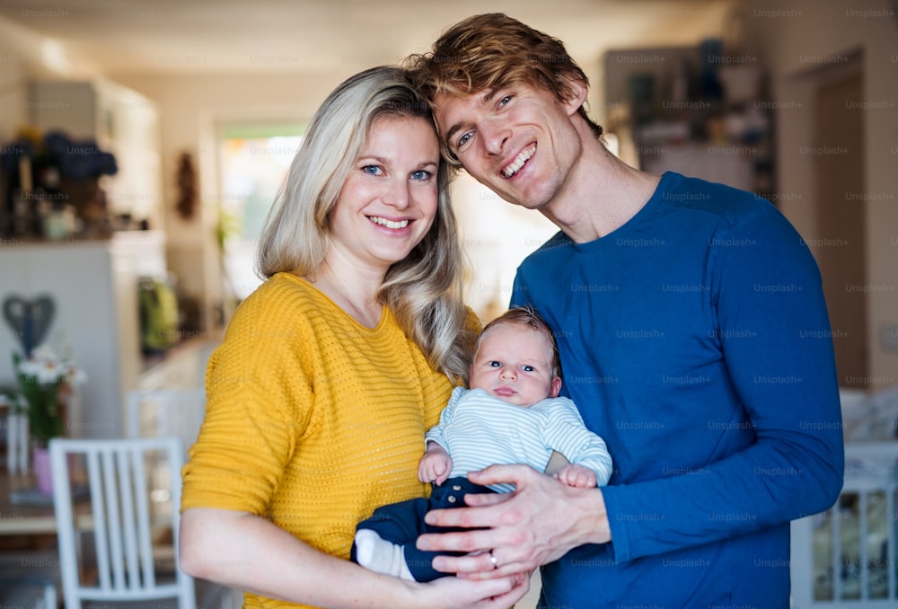 A front view portrait of beautiful young parents with a newborn baby at home.