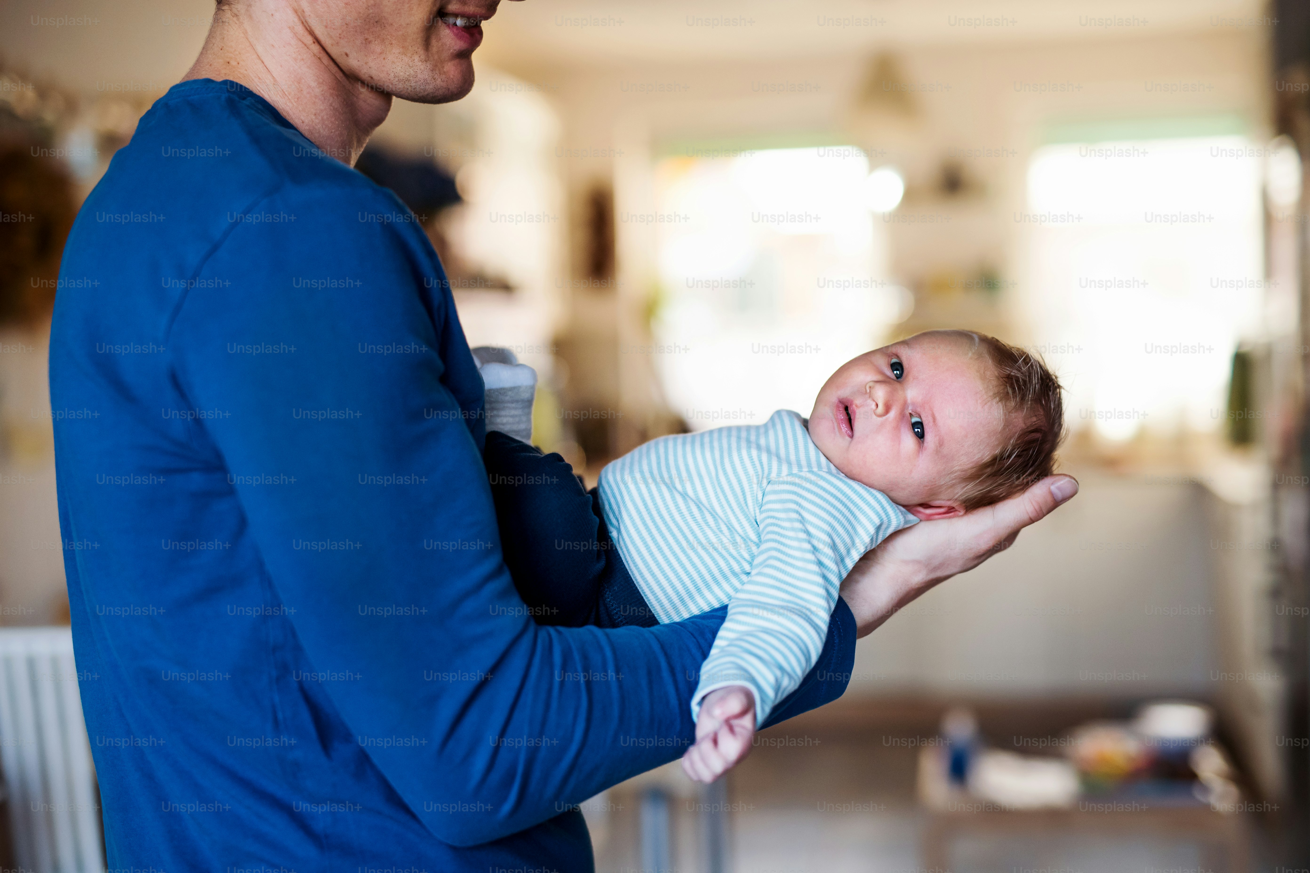 A midsection of young father holding a newborn baby at home.