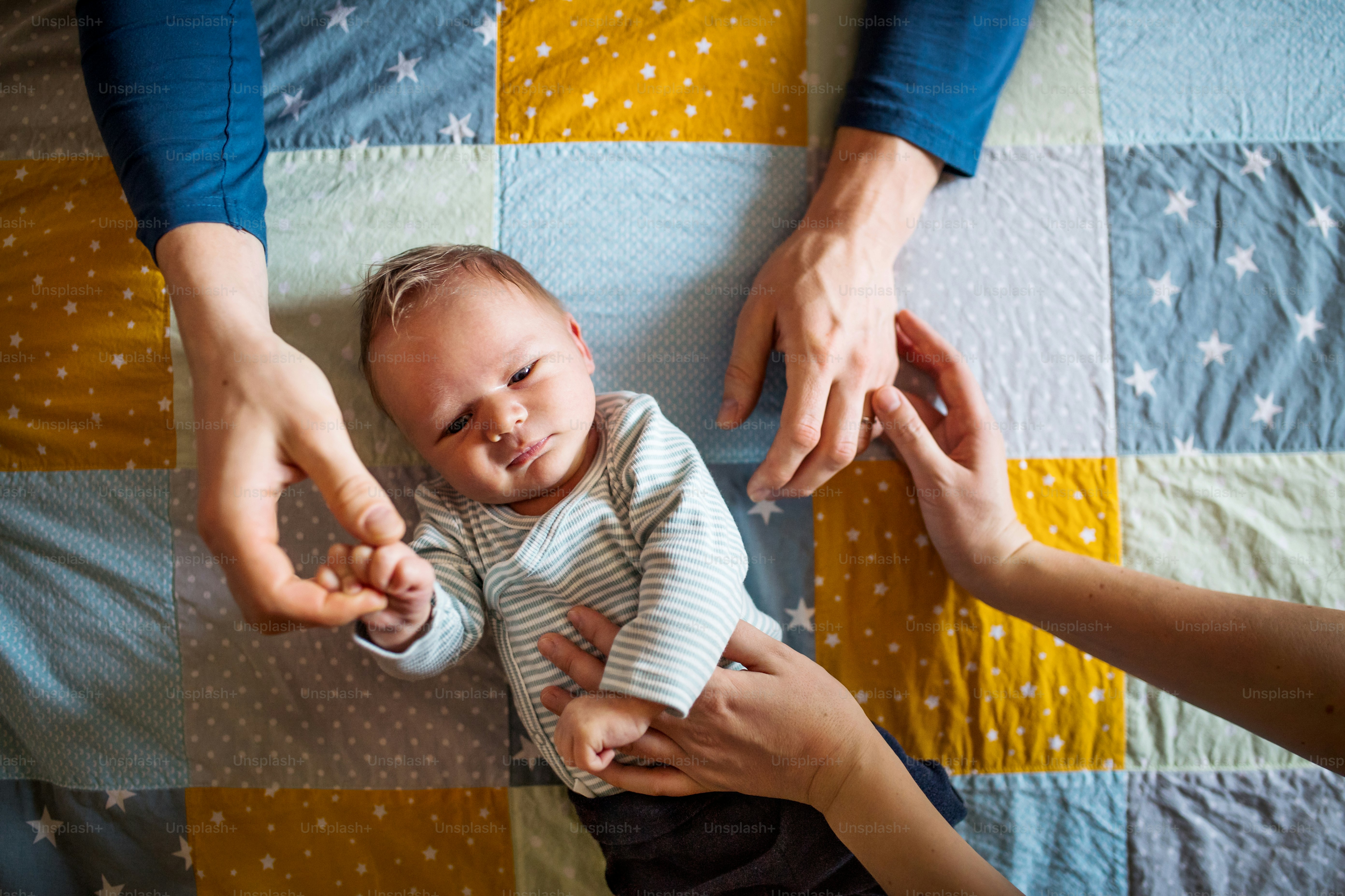 A top view of a newborn baby lying on bed on a quilted blanket at home.