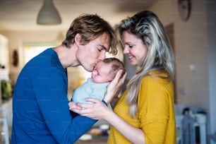 Belos pais jovens segurando um bebê recém-nascido em casa, beijando.