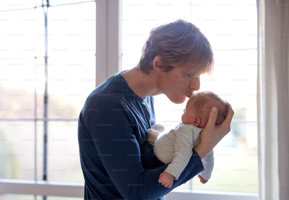 A happy young father holding a newborn baby at home, kissing him.