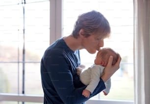 A happy young father holding a newborn baby at home, kissing him.