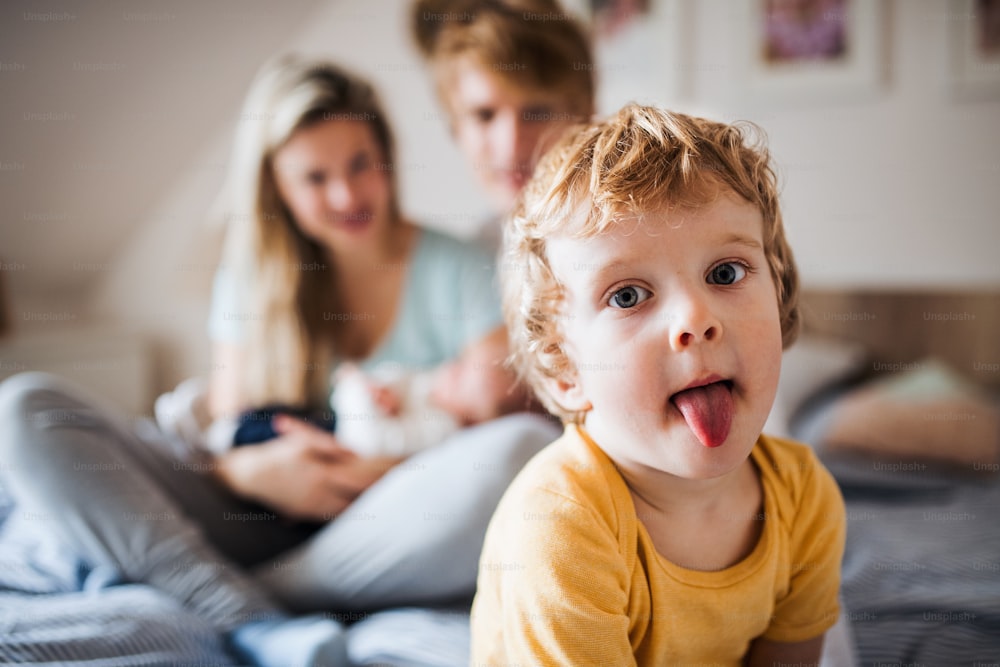 A small toddler boy with parents and newborn baby at home, sticking tongue out.