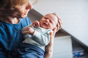 A close -up of young father holding a crying newborn baby at home.