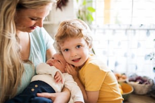 Una bella giovane madre con un neonato e suo fratello piccolo a casa.